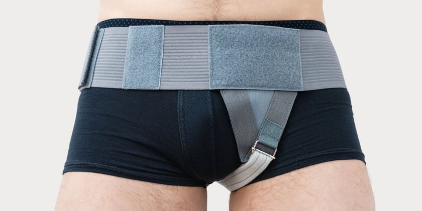 Ein junger Mann mit schwarzer Unterhose trägt einen Herniengurt. 